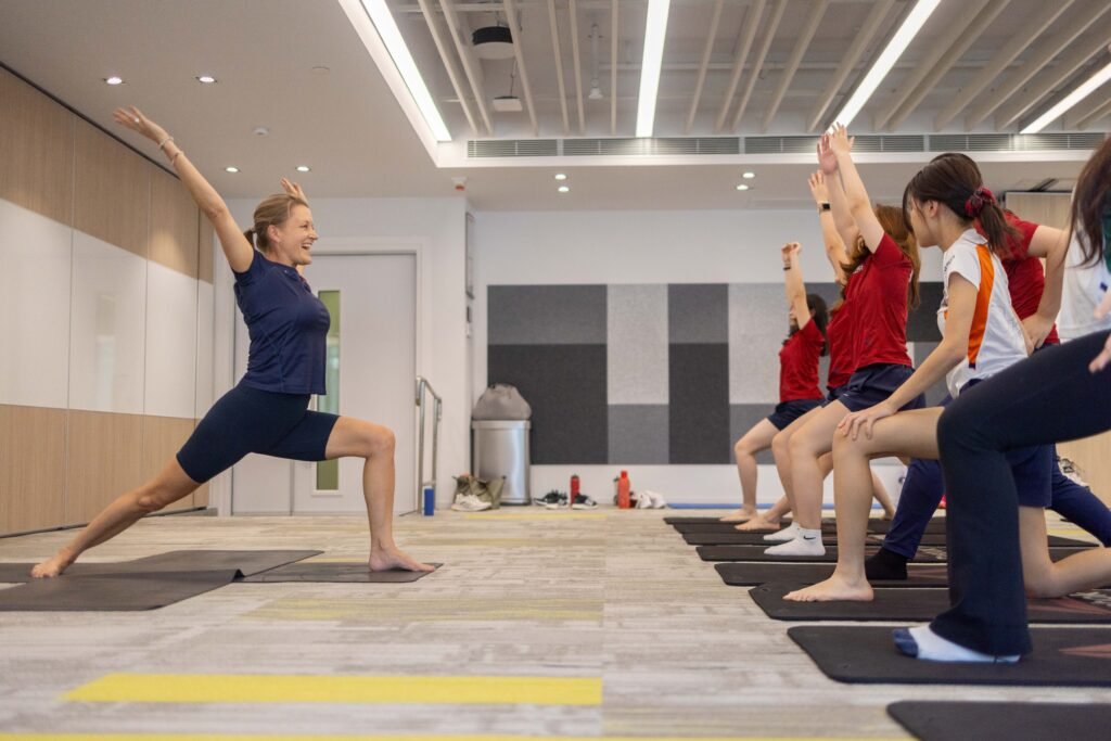 Teenagers practicing yoga in a school campus setting at Kellett International School, demonstrating a sun salutation pose with Rowena Hunt